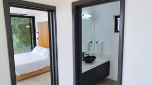 Une chambre d’hôtel moderne avec un grand lit, une salle de bain dotée d’un lavabo noir et une vue sur la verdure.