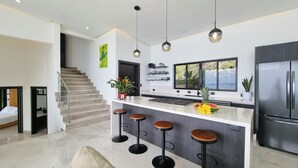Une cuisine moderne dotée d’un îlot central, de tabourets de bar, d’un réfrigérateur et d’un escalier menant à un autre niveau.