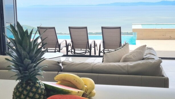 Une chambre avec vue sur l’océan, une piscine et une table garnie de fruits.