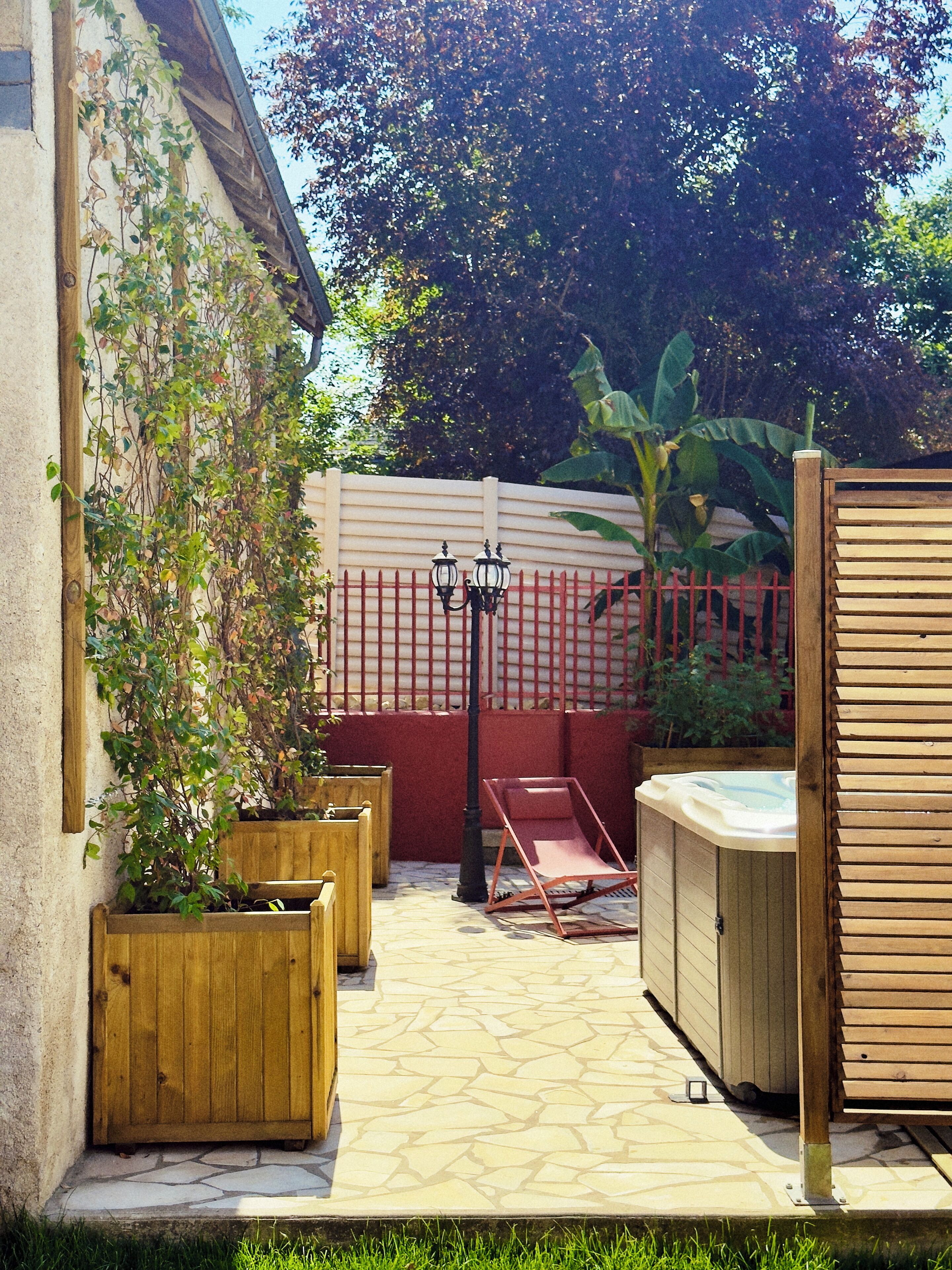 A patio area with a wooden fence, a hot tub, and planters.