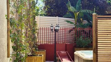 A patio area with a wooden fence, a hot tub, and planters.