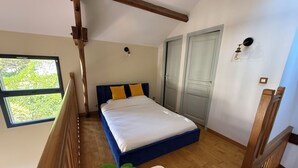 A bedroom with a bed, wooden floor, a window, and a plant. - La Maison sous les Arbres: duplex, garden & spa ⎮ Touraine & Amboise (Pocé-sur-Cisse)