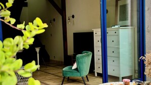 A room with a green armchair, a white dresser, a tiled floor, and a small table with food items. - La Maison sous les Arbres: duplex, garden & spa ⎮ Touraine & Amboise (Pocé-sur-Cisse)