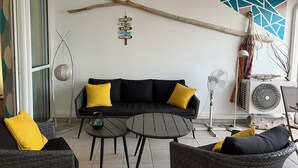 A modern living room with a black sofa, yellow cushions, a round table, wicker chairs, a hanging branch decoration, and a wall-mounted sign with directional phrases. - Le Lagon 11 - Large T2 Sea and Bay View - SAINTE LUCE (Sainte-Luce)