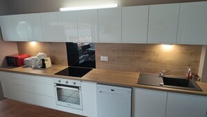 A compact kitchen with white cabinets, a built-in oven, a dishwasher, a sink, and a countertop with a coffee maker and other appliances. - Le Lagon 11 - Large T2 Sea and Bay View - SAINTE LUCE (Sainte-Luce)