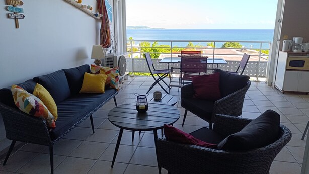 A living room with a sofa, armchairs, and a coffee table. There is a balcony with a view of the sea. - Le Lagon 11 - Large T2 Sea and Bay View - SAINTE LUCE (Sainte-Luce)
