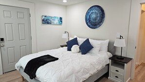 Une chambre à coucher avec un lit, deux tables de chevet, une lampe fixée au mur et une porte.