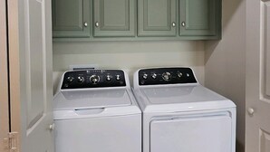 Une buanderie équipée de deux machines à laver à chargement frontal et de meubles de rangement verts placés au-dessus.
