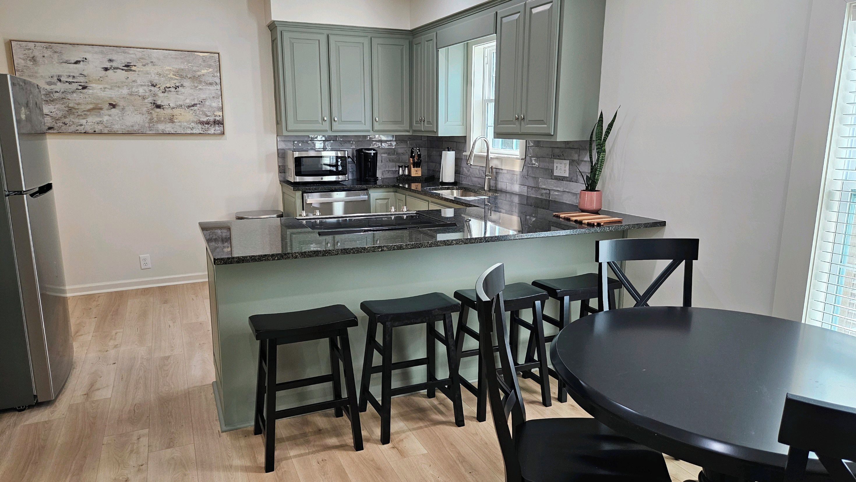 A modern kitchen with a central island, bar stools, and a dining table.