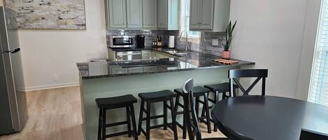 A modern kitchen with a central island, bar stools, and a dining table.