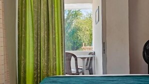 Ein Zimmer mit einem Bett, einer Schiebetür zu einem Außenbereich mit Tisch und Stühlen sowie einem Ventilator.