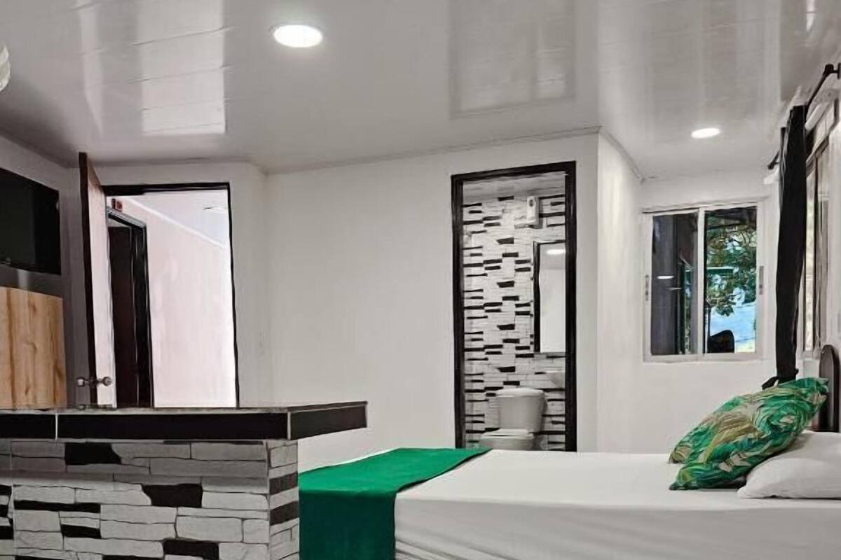 A modern bedroom with a large bed, a green bedside table, a white bathtub, and a window with curtains.