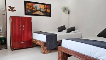 Quarto com duas camas, um guarda-roupa vermelho, um quadro e um ventilador.