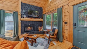 A cozy cabin interior with a stone fireplace, wooden walls, and a comfortable seating area.