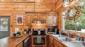 A wooden cabin-style kitchen with a stainless steel stove, a microwave, and a sink.