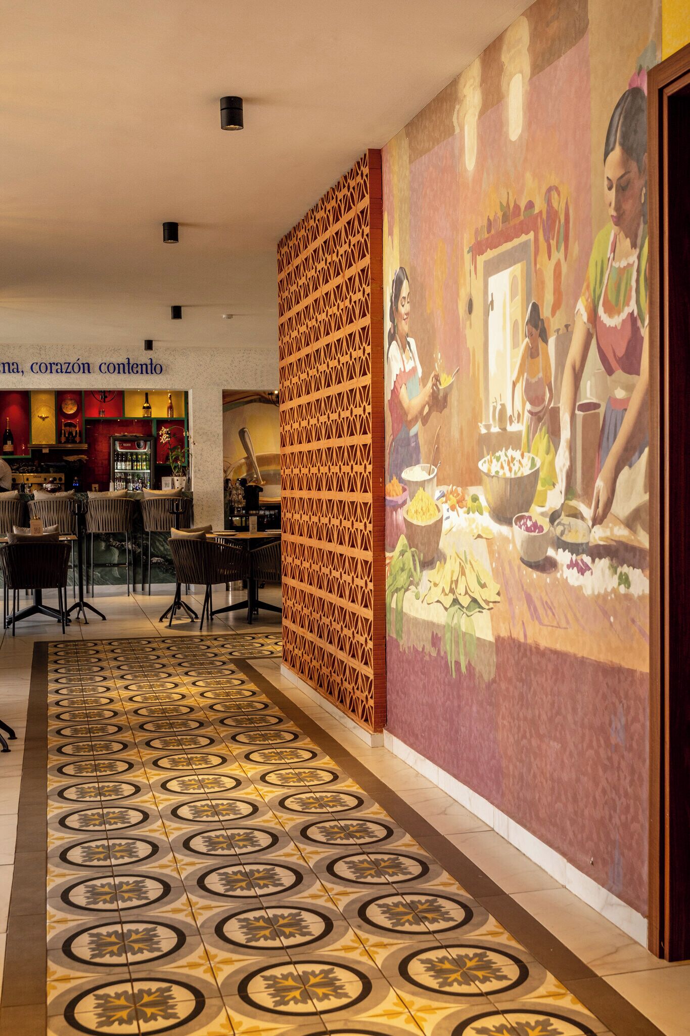 A hotel lobby with a patterned floor, a bar area, and a mural depicting a dining scene.
