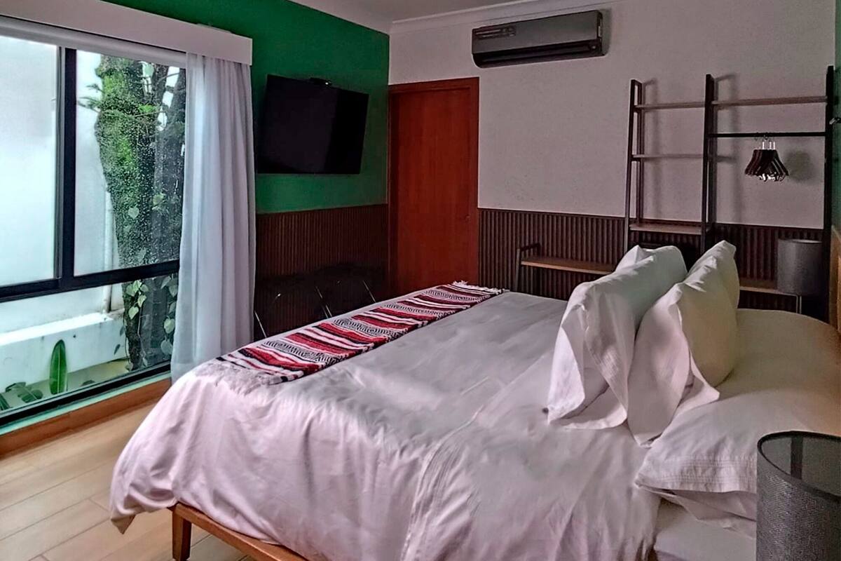 A bedroom with a bed, a TV mounted on the wall, and a window with curtains.