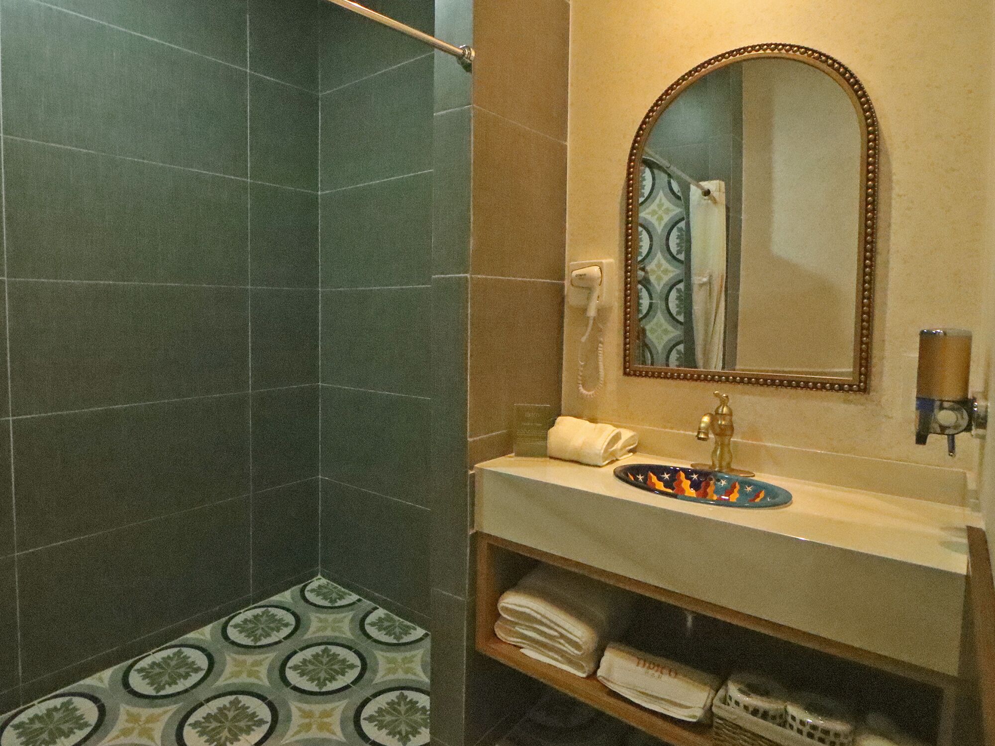 Een badkamer met een douche, een wastafel met decoratieve kom, een spiegel met decoratieve lijst en een handdoekhouder.