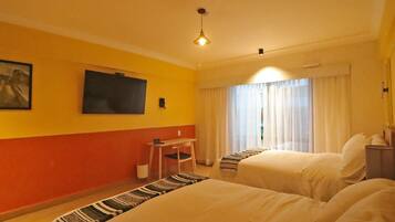 A hotel room with two beds, a desk, a chair, a television, and a window with curtains.