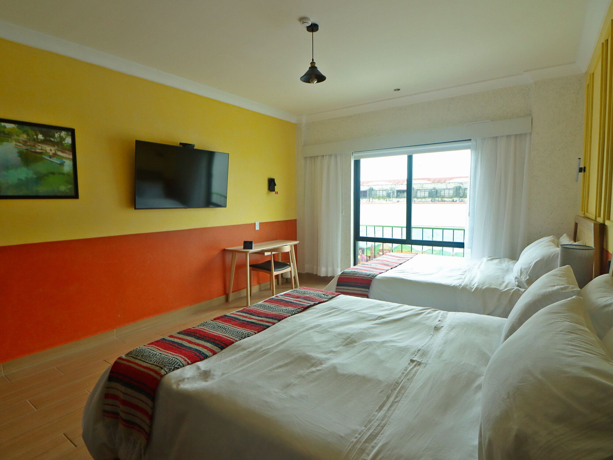 A hotel room with two beds, a desk, a TV, and a balcony with a view.