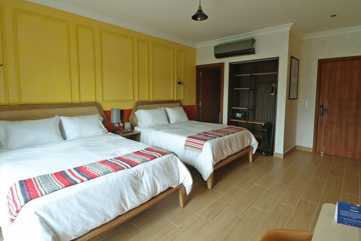 A hotel room with two beds, a wooden floor, a yellow wall, a ceiling fan, and a door.