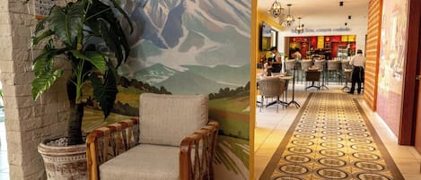 A lobby with a large mural, a seating area with a chair, a potted plant, and a patterned floor.