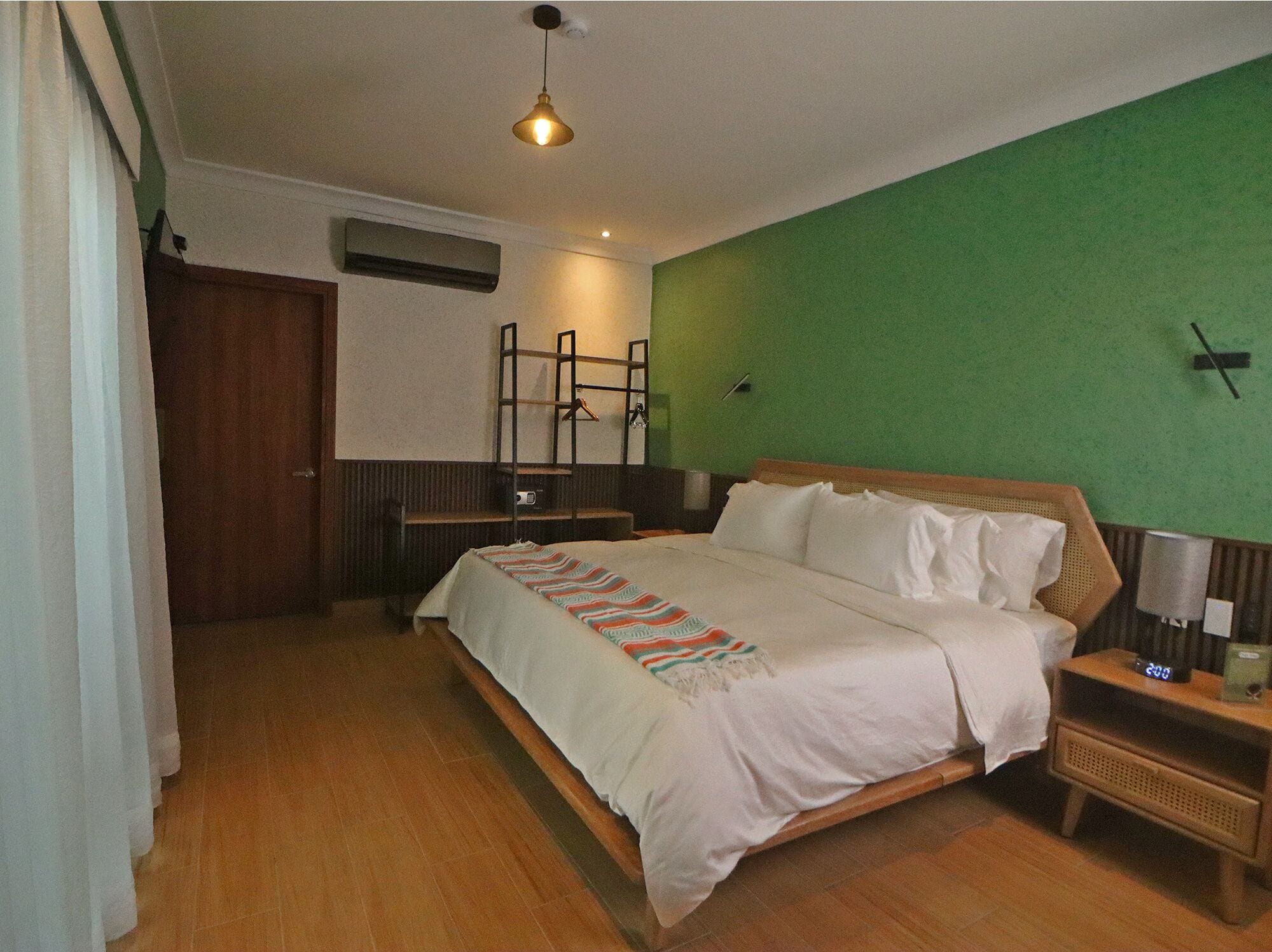 Una habitación de hotel con una cama, una mesita de noche, una lámpara, un reloj y una pared verde.
