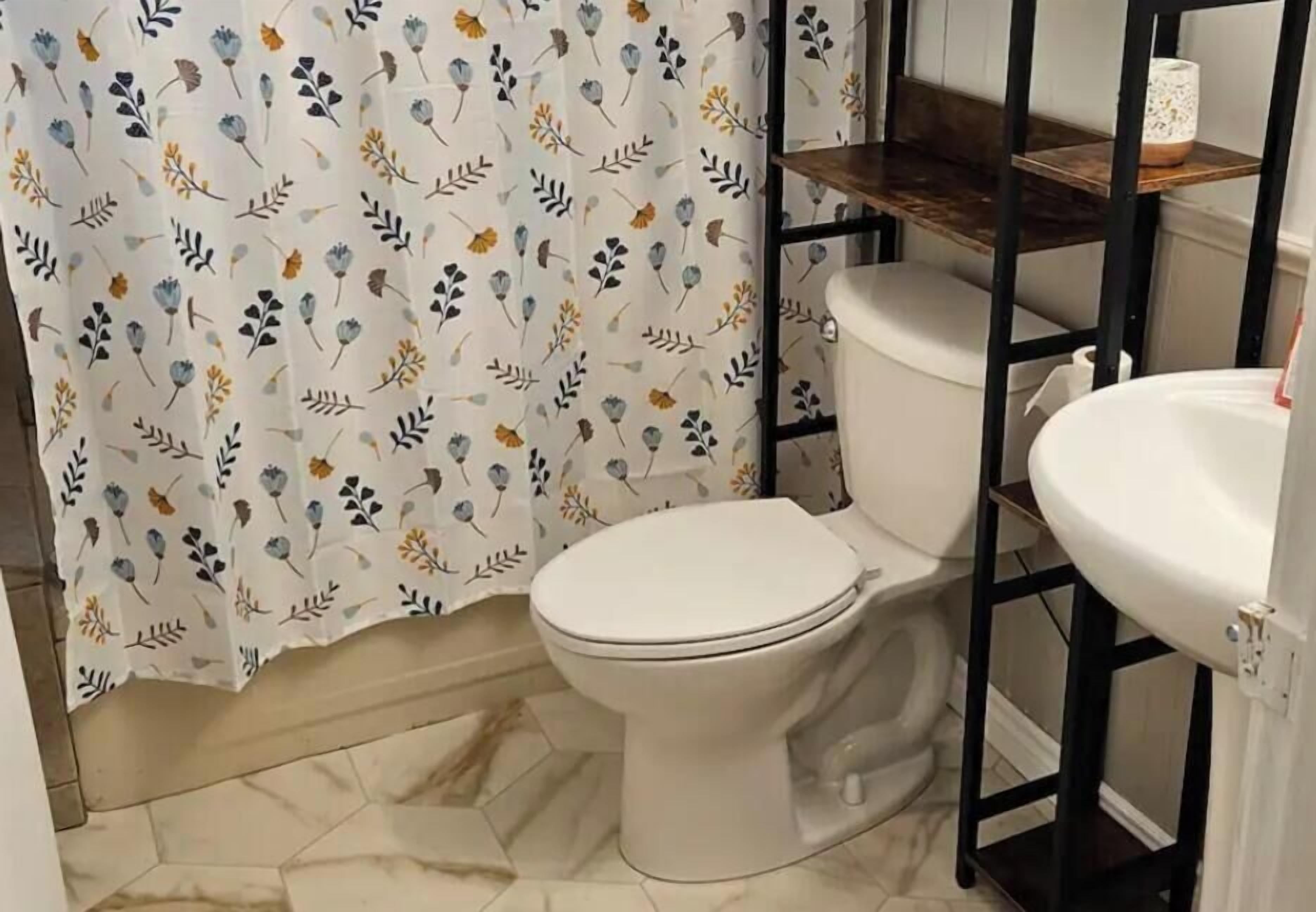 Un baño con inodoro, lavamanos y cortina de ducha estampada con motivos florales.