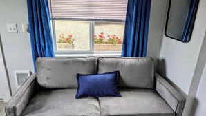 Un sofá gris con un cojín azul frente a una ventana con cortinas azules.