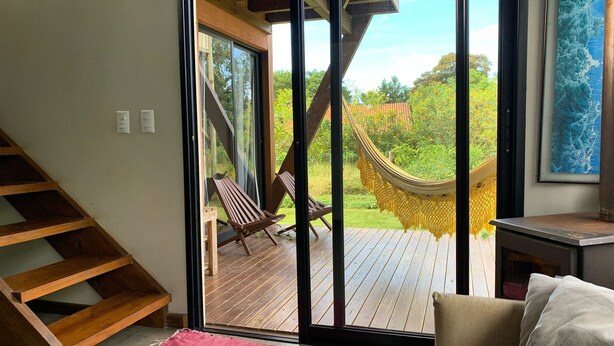 Ein Zimmer mit einer Holztreppe, einer Hängematte, einer Holzdiele und Blick auf einen Garten.