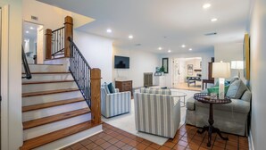 A spacious living area with a wooden staircase, a gray sofa, a striped armchair, and a small round table.