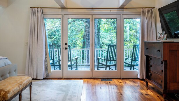A room with a large sliding glass door leading to a balcony with chairs, a bench, and a wooden dresser.