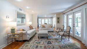 A spacious living room with a large window, a patterned rug, and a mix of seating including a sofa and armchairs.