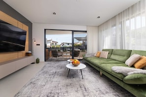 Un salon moderne avec un canapé vert, un téléviseur à écran plat et un coin repas comprenant des chaises et une table.
