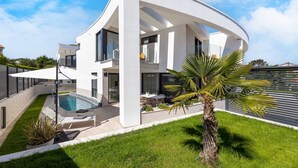 Une maison moderne à deux étages, dotée d’une piscine, d’un espace extérieur aménagé et d’une pelouse bien entretenue.