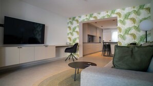 A modern living room with a flat-screen TV, a sofa, a coffee table, and a dining area with a kitchen in the background.