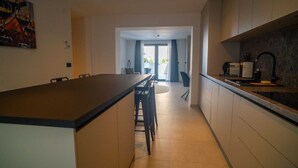 A modern kitchen with a central island, a dining area with chairs, and a view to a balcony.