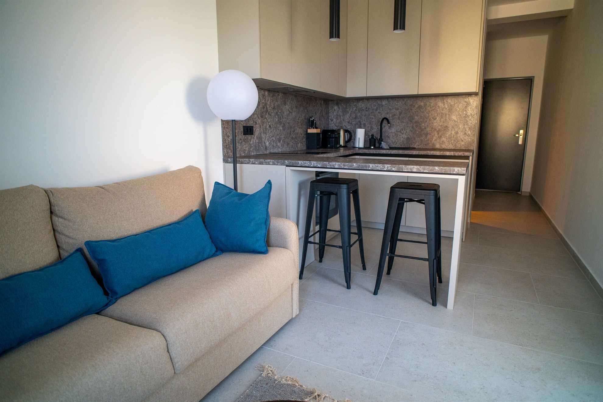 A modern kitchen with a built-in island, a sofa with blue cushions, and two bar stools.