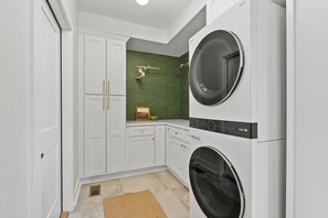 A laundry room with stacked washers and dryers, white cabinetry, a green accent wall, and a small picture frame.
