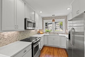 A modern kitchen with white cabinets, a stainless steel refrigerator, a microwave, and a wooden floor.