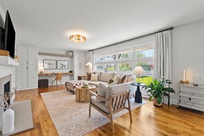 A modern living room with a sofa, armchairs, a coffee table, and a fireplace. There is a large window with curtains, a dining area with a table and chairs, and a kitchen area with cabinets and a countertop. - 🐴🏠 CHARMING DOWNTOWN GEORGETOWN 3-bed/2-bath home. Professionally decorated. (Georgetown)