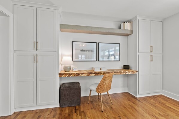 A kitchen with white cabinets, a wooden countertop, a woven chair, and a small ottoman.