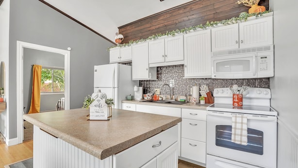 A kitchen with white cabinetry, a central island, a microwave, an oven, and a window with a view.