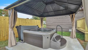 A hot tub under a covered patio with a wooden fence in the background.
