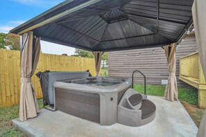 Un bain à remous sous une terrasse couverte, avec une clôture en bois en arrière-plan.