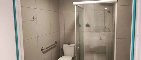 A small, modern bathroom with a toilet, a glass shower enclosure, and a grab bar.