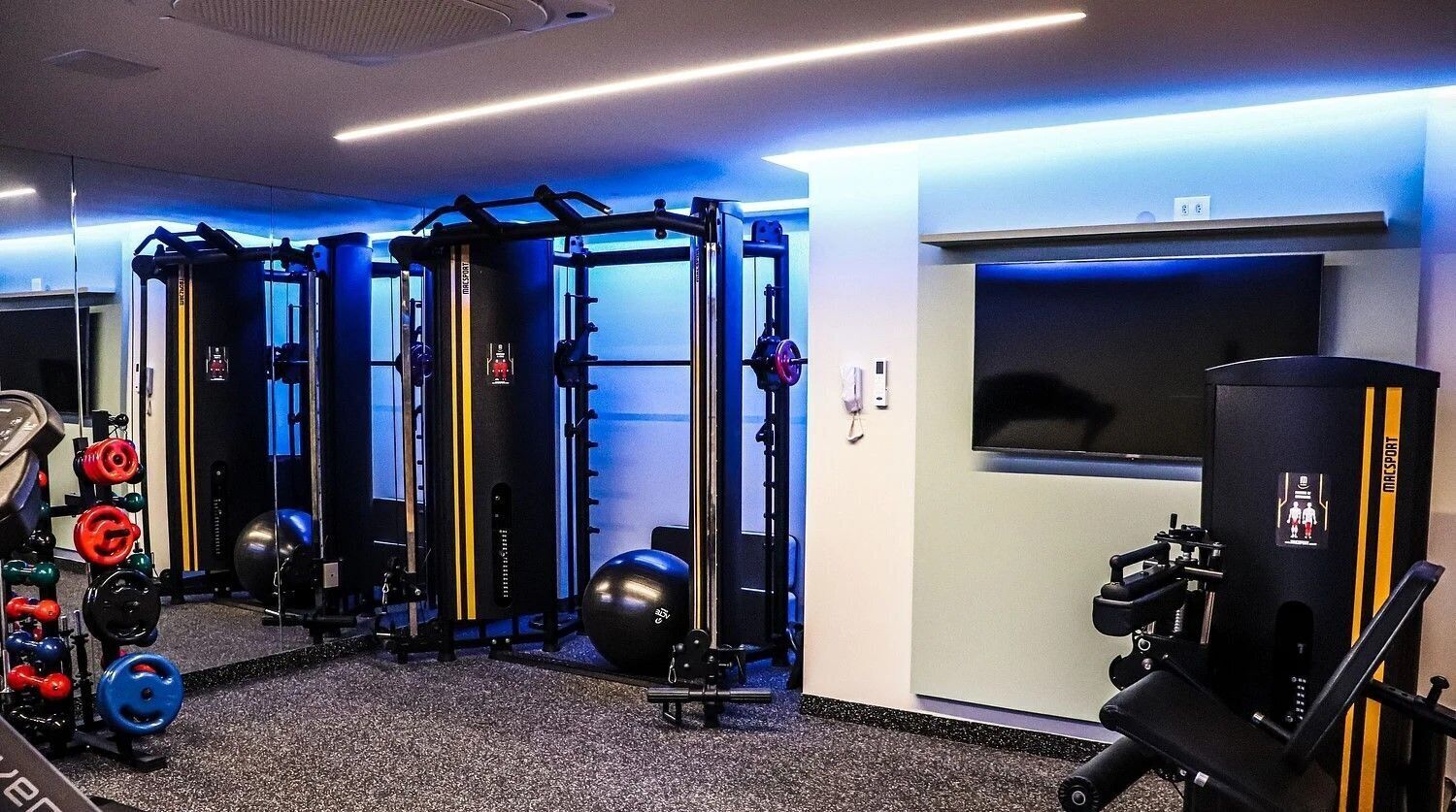 A gym with weightlifting equipment, exercise balls, and a television screen.
