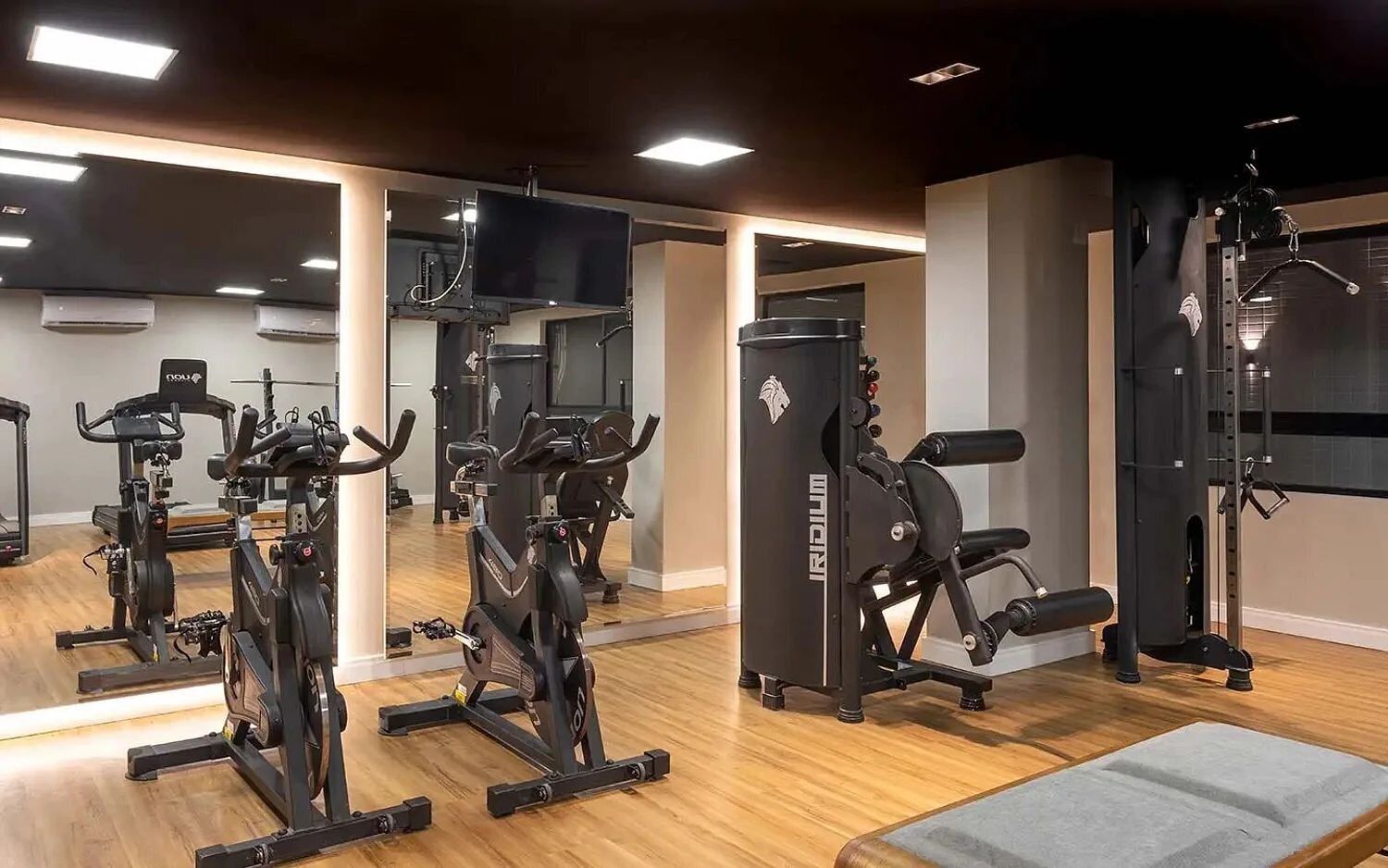 A gym with exercise equipment, mirrors, and a wooden floor.
