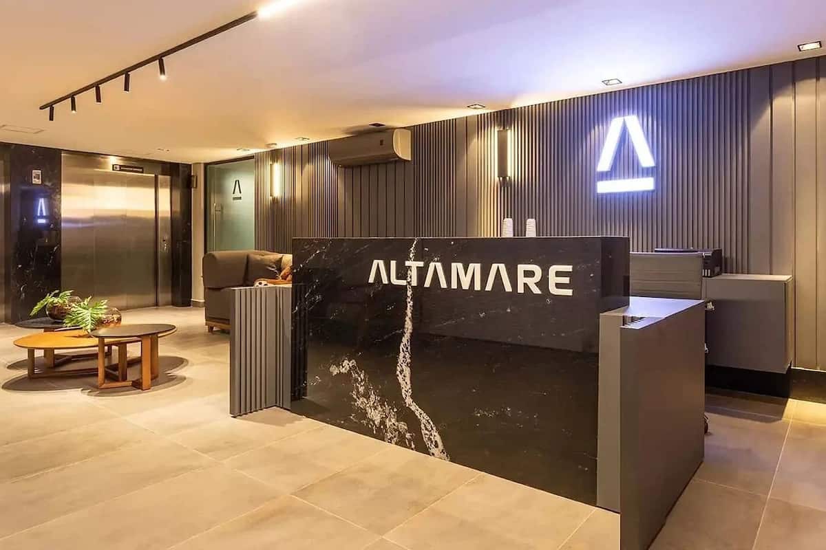 Una recepción con letrero 'ALTAMARE', un interior moderno con un sofá y una mesita, y una gran letra 'A' en la pared.