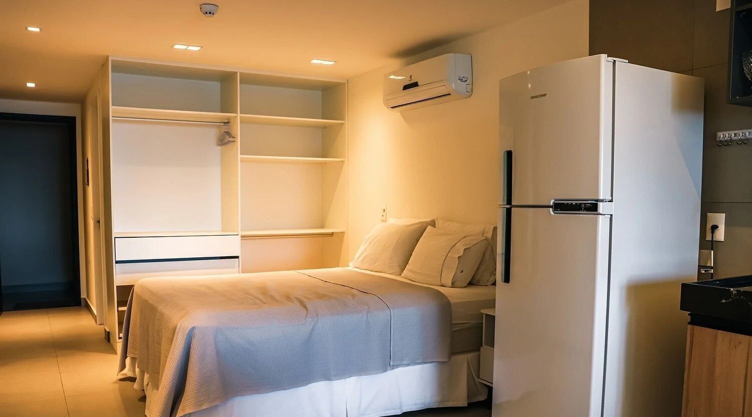 A bedroom with a bed, a white wardrobe, and a white refrigerator.